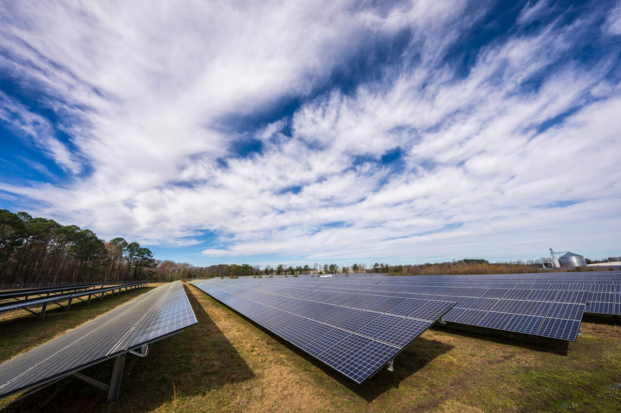 Solar panels spread across a field under a bright blue sky with clouds, showcasing renewable energy.
